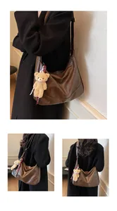 Detail view of dark brown leather shoulder bag with cute teddy bear charm and ribbon
