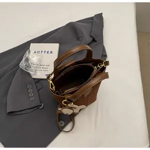 Detailed view of brown suede bucket bag with cute bear charm on gray blazer background