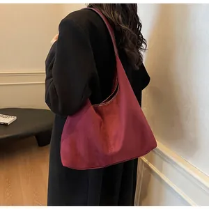 Close-up of burgundy hobo bag in matte suede worn on shoulder with black coat