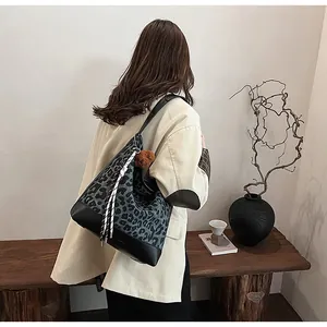 Lifestyle shot of large leopard print tote bag with plush bear charm and tassel details