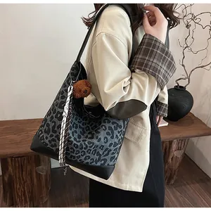 Detail of large leopard print tote bag featuring a plush bear charm and black leather straps