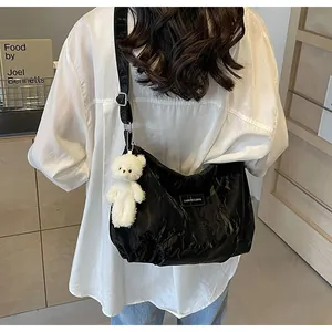 Detail einer glänzenden schwarzen Samt-Tote-Bag mit einem weißen Plüschbär-Anhänger am Schultergurt