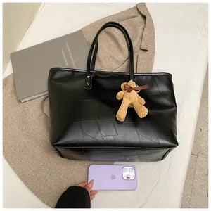 Detail of black patchwork leather tote with plush bear charm and long shoulder straps