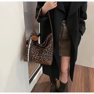 Detail of leopard print tote bag with brown leather trim and plush ball pendant