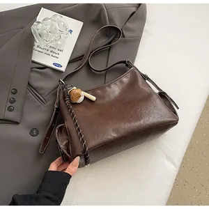 Dettaglio della borsa a secchiello marrone scuro vintage con cuciture e ciondolo orso