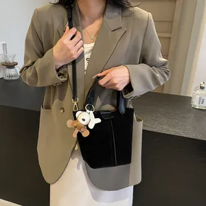 Fashionable black bucket bag with bear pendant shown on model in modern cafe setting