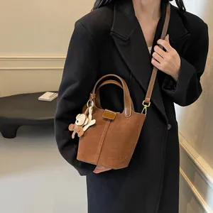 Brown suede bucket bag with leather strap and bear charm shown on a fashion model
