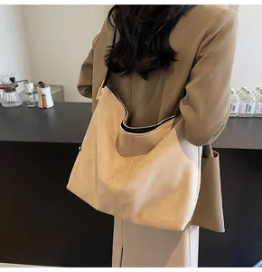 Detail of camel suede tote bag with golden hardware shown on shoulder in a cafe setting
