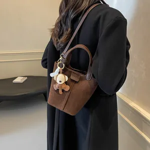 Brown suede bucket bag with stylish top handle and cute charm on black coat