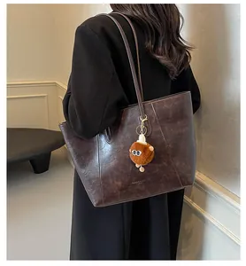 Sac fourre-tout en cuir marron foncé avec breloque en peluche, porté par un mannequin chic