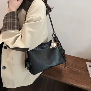 Elegante borsa a secchiello nera con charm da baseball e dettagli intrecciati in vista laterale
