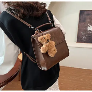 Detail of vintage brown PU leather backpack with METI SHI HANG embossed logo and bear charm