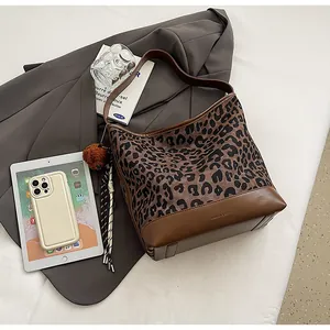 Detail view of leopard print tote bag with leather base and plush bear charm accessory