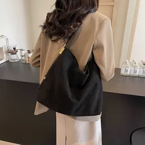 Black suede tote bag with brown straps and gold hardware worn by a model in a suit