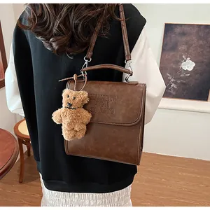 Detail view of brown vintage leather bag with debossed text and plush bear charm