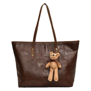 Brown leather tote bag with large capacity and cute bear pendant on white background