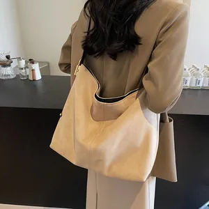 Minimalist large beige suede tote bag with metal buckle shown from a side view on a model