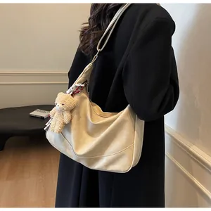 Detail of hobo shoulder bag featuring a teddy bear charm and striped scarf decoration