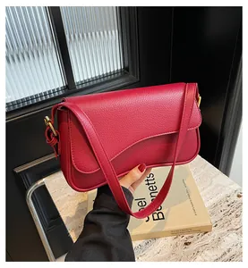 Detail of red lychee pattern leather shoulder bag with a gold metal buckle and strap