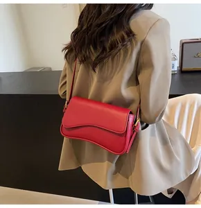 Detail of burgundy pebbled leather handbag with wavy flap and gold hardware on model