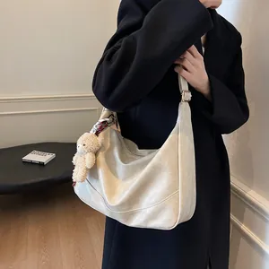 Chic beige crescent shoulder bag with plush charm and silk scarf detail on black coat