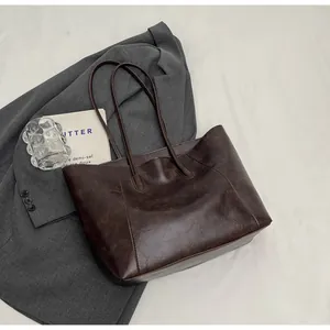 Détail d'un sac cabas en similicuir marron foncé avec texture vintage sur un blazer gris