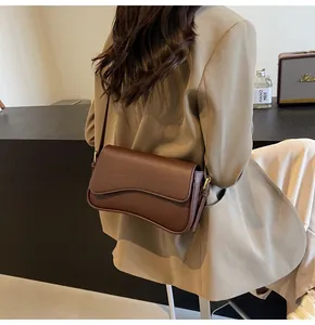 Detail view of brown pebble leather crossbody bag featuring wave-cut flap and gold hardware