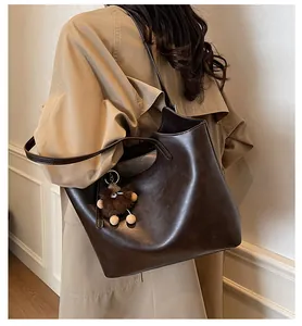Detail of dark brown leather tote bag with furry charm shown on a trench coat model