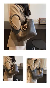 Detail of vintage brown leather tote bag featuring a cute plush monster charm and embossed text