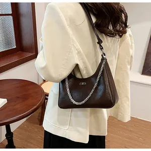 Detail of dark brown glossy cracked leather bag with silver chain on model arm