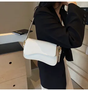 Detail of white lychee leather bag featuring a wavy flap and gold buckle on black blazer