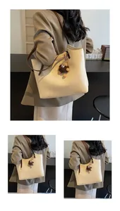 Detail of a beige tote bag with a brown monster plush charm and slim straps for work