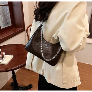 Dark brown leather underarm bag with silver chain worn by a model in a beige corduroy suit