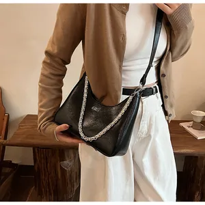 Detail of black leather hobo bag with silver chain and metal logo in lifestyle setting