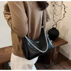 Detail of black leather underarm bag with silver chain and metal logo on a model