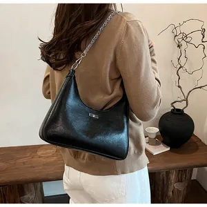 Model wearing a black cracked leather underarm bag with silver chain in minimalist room