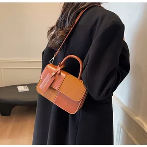 Detalle de bolso bandolera bicolor en ante marrón y cuero liso con colgante