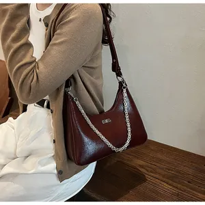 Detail of burgundy cracked leather underarm bag with silver chain and logo tag