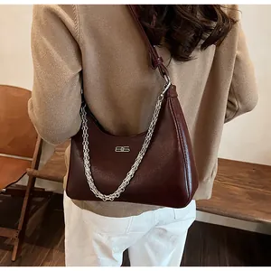 Detail of dark burgundy underarm bag with cracked leather texture and silver chain strap