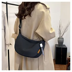 Détail du sac bandoulière noir en forme de croissant avec étiquette orange et cordon blanc