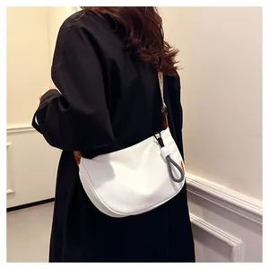 Détail d'un sac bandoulière blanc en demi-lune avec sangle large texturée et pendentif corde