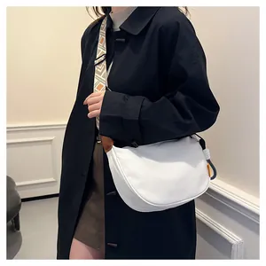 Sac demi-lune blanc avec bandoulière géométrique porté sur un manteau noir