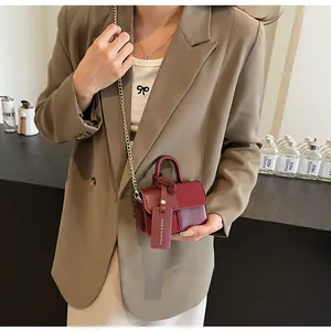Detalle de mini bolso cuadrado granate con cadena dorada y etiqueta de moda al hombro