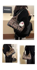 Detail of leopard print tote bag featuring black straps and a white plush dog charm accessory