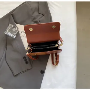 Detalle de bolso bandolera de cuero marrón con hebillas magnéticas doradas y bolsillo interior con cremallera