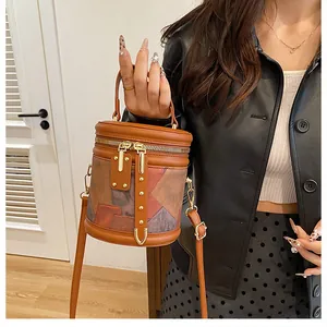 Detail view of stylish patchwork cylinder bucket bag with gold hardware and dual zippers