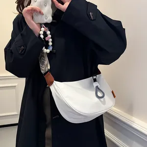 Sac croissant blanc minimaliste avec bandoulière tissée et breloque sur manteau noir