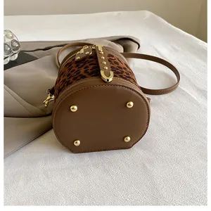 Detailed view of leopard print bucket bag with gold-tone base studs and brown leather trim