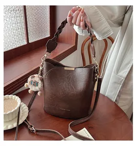 Detail der braunen Beuteltasche mit geflochtenem Griff und weißem Anhänger auf Holztisch