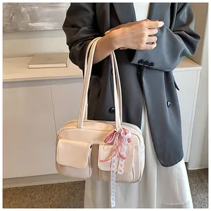 Detail of cream tote bag featuring decorative front pockets and red checkered bow charm